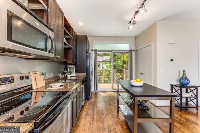 kitchen with dark brown cabinetry, sink, stainless steel appliances, dark stone counters, and light wood-type flooring