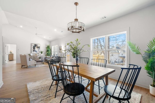 dining room with ceiling fan with notable chandelier, light hardwood / wood-style floors, and lofted ceiling