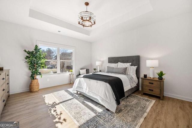 bedroom featuring light wood-type flooring, a raised ceiling, and a notable chandelier