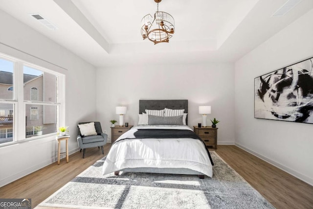 bedroom featuring a tray ceiling, multiple windows, hardwood / wood-style floors, and a chandelier