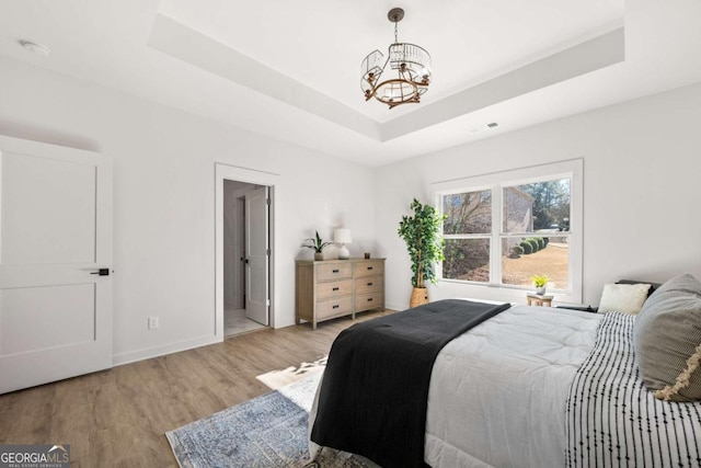 bedroom with a chandelier, light wood-type flooring, and a tray ceiling