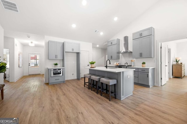 kitchen with sink, wall chimney exhaust hood, an island with sink, a breakfast bar area, and gray cabinets