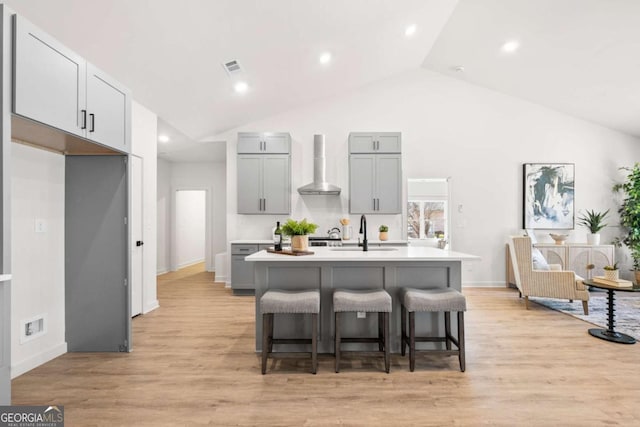 kitchen featuring a center island with sink, a kitchen breakfast bar, wall chimney range hood, sink, and light hardwood / wood-style floors