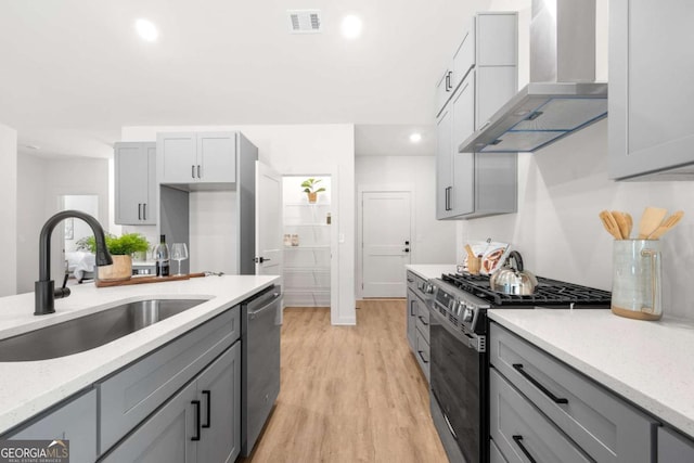 kitchen featuring gray cabinetry, stainless steel appliances, sink, wall chimney range hood, and light hardwood / wood-style flooring