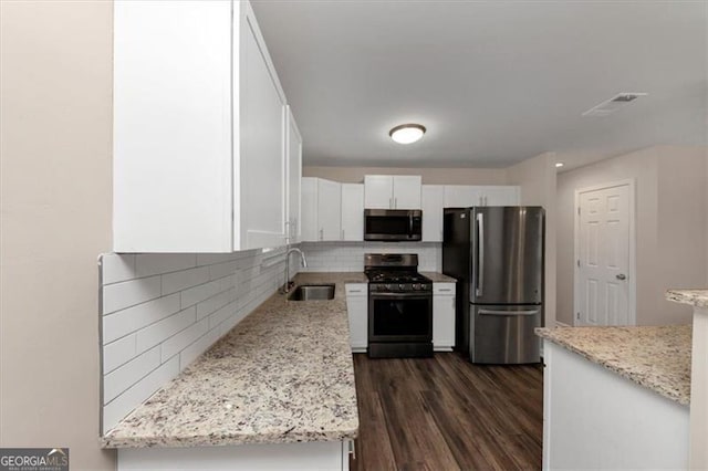 kitchen with light stone countertops, backsplash, stainless steel appliances, sink, and white cabinetry