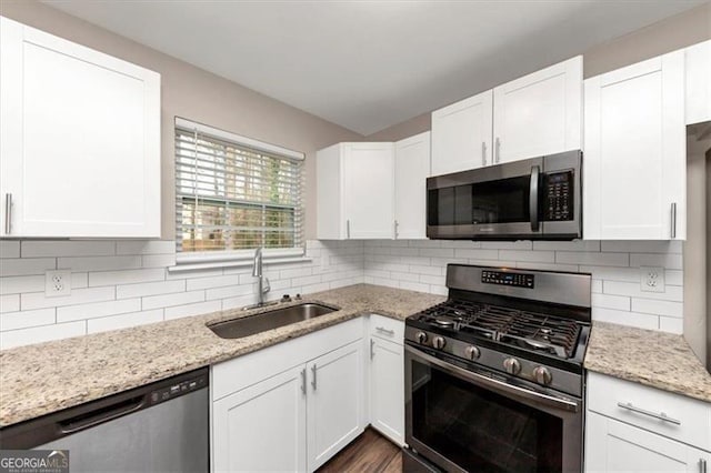 kitchen featuring white cabinets, appliances with stainless steel finishes, light stone counters, and sink