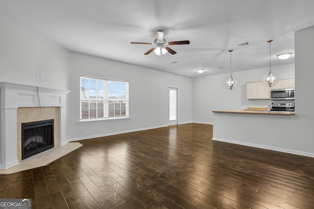 unfurnished living room featuring dark hardwood / wood-style floors, ceiling fan, and a tiled fireplace