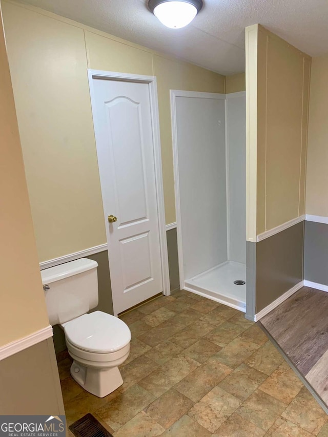 bathroom featuring toilet, a shower, and a textured ceiling