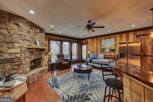 living room featuring ceiling fan, wood-type flooring, a stone fireplace, and wooden walls