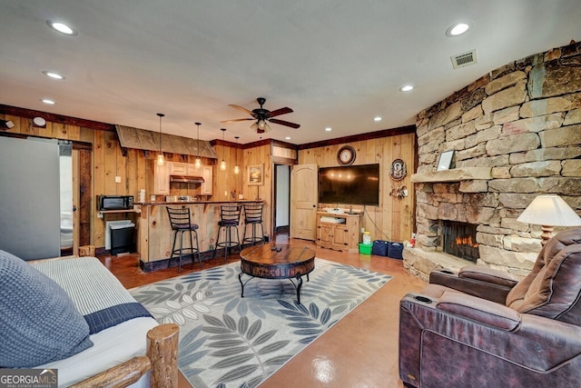 living room with ceiling fan, wooden walls, and a fireplace