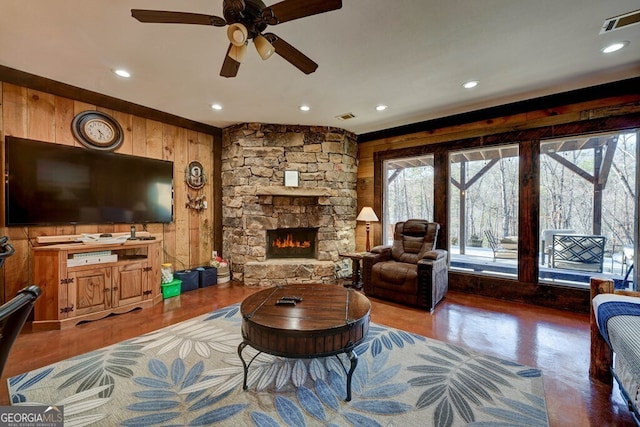 living room with ceiling fan, a stone fireplace, and wood walls