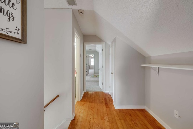 hall with a textured ceiling, light hardwood / wood-style flooring, and lofted ceiling