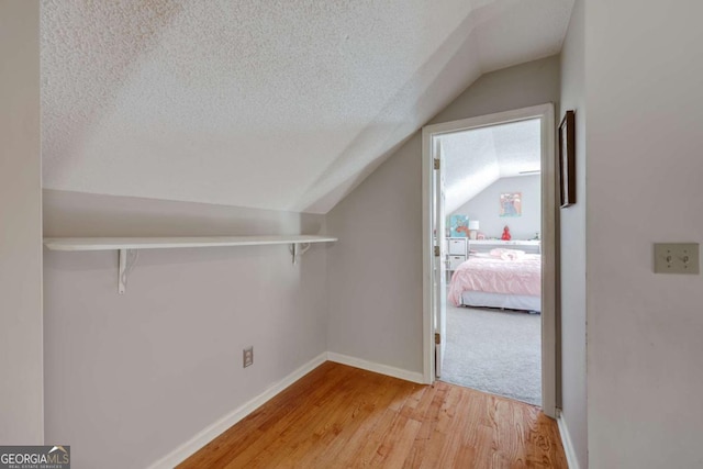 additional living space featuring a textured ceiling, light hardwood / wood-style flooring, and lofted ceiling