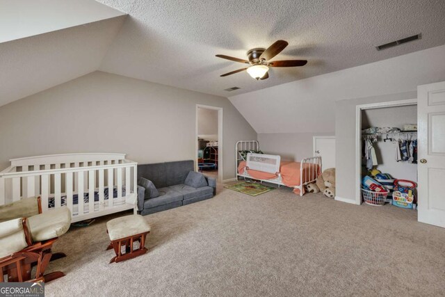 bedroom featuring a textured ceiling, vaulted ceiling, ceiling fan, a nursery area, and a closet