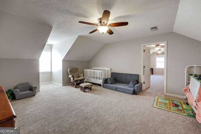 carpeted bedroom with a crib, a textured ceiling, multiple windows, and ceiling fan