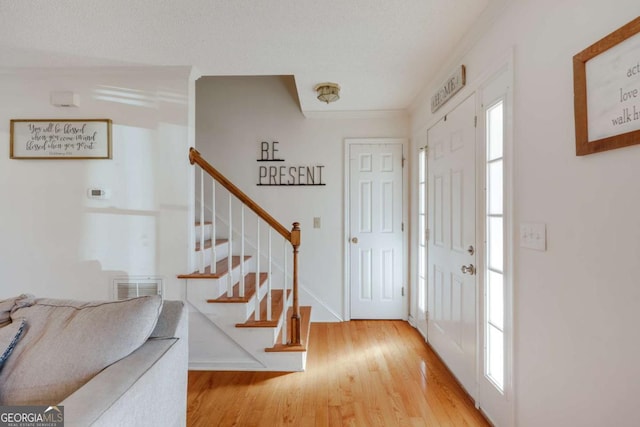 entryway featuring crown molding, a textured ceiling, and light hardwood / wood-style flooring