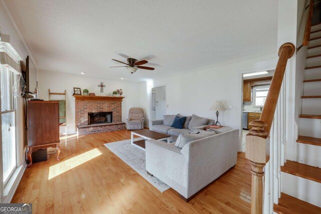 living room featuring a healthy amount of sunlight, ceiling fan, light hardwood / wood-style floors, and a brick fireplace