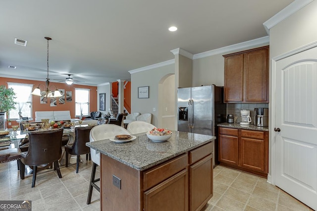 kitchen featuring dark stone countertops, stainless steel fridge, pendant lighting, a breakfast bar, and a kitchen island