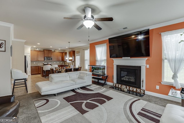 carpeted living room featuring plenty of natural light, ceiling fan, and crown molding