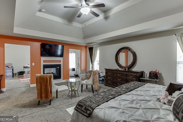 carpeted bedroom with a raised ceiling, ceiling fan, and a multi sided fireplace