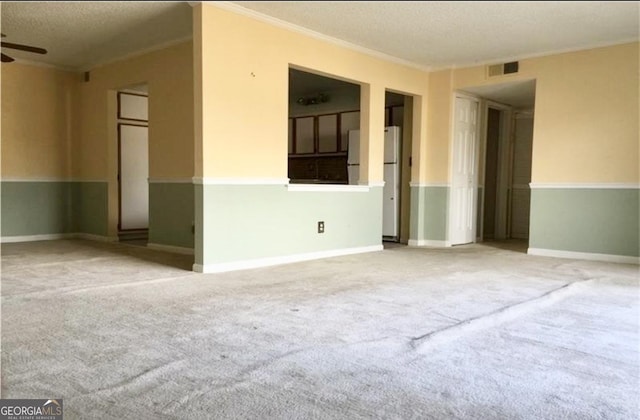 carpeted empty room featuring ceiling fan, crown molding, and a textured ceiling