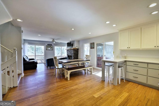 kitchen featuring white cabinetry, ceiling fan, light hardwood / wood-style flooring, kitchen peninsula, and a fireplace