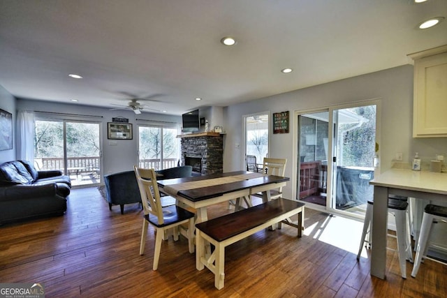 dining area with dark hardwood / wood-style flooring, ceiling fan, a stone fireplace, and a healthy amount of sunlight