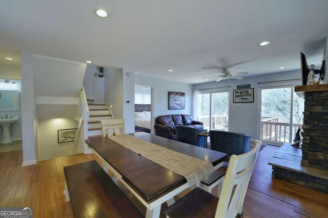 dining room featuring hardwood / wood-style floors, ceiling fan, a stone fireplace, and sink