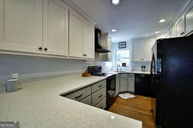 kitchen with sink, white cabinets, black appliances, and wall chimney range hood