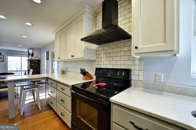 kitchen with wall chimney range hood, black electric range oven, decorative backsplash, white cabinets, and light wood-type flooring