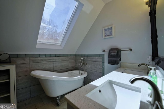 bathroom featuring vanity, a bathtub, tile walls, and vaulted ceiling with skylight