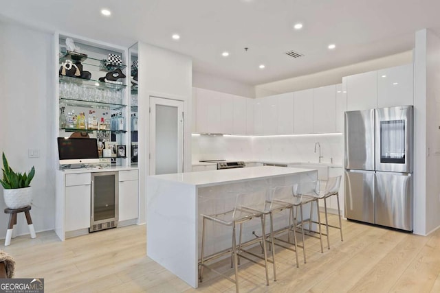 kitchen with white cabinetry, wine cooler, light hardwood / wood-style flooring, stainless steel fridge, and a kitchen island