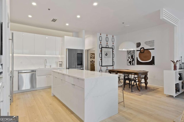 kitchen with white cabinets, a kitchen island, stainless steel appliances, and light hardwood / wood-style flooring