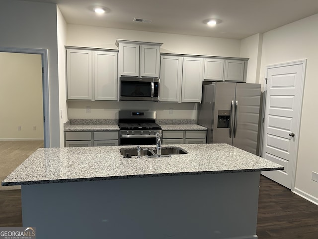 kitchen with stainless steel appliances, an island with sink, sink, and light stone counters