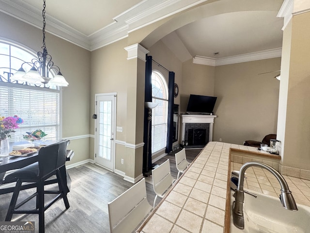 kitchen featuring hanging light fixtures, wood-type flooring, tile countertops, crown molding, and a brick fireplace