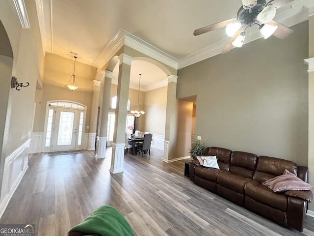 living room featuring decorative columns, hardwood / wood-style flooring, a high ceiling, ornamental molding, and ceiling fan with notable chandelier