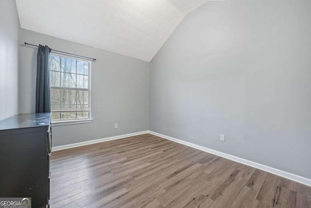 unfurnished room featuring a textured ceiling, hardwood / wood-style floors, and vaulted ceiling