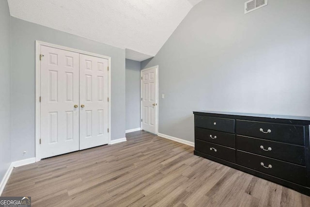 unfurnished bedroom with a textured ceiling, light hardwood / wood-style floors, vaulted ceiling, and a closet