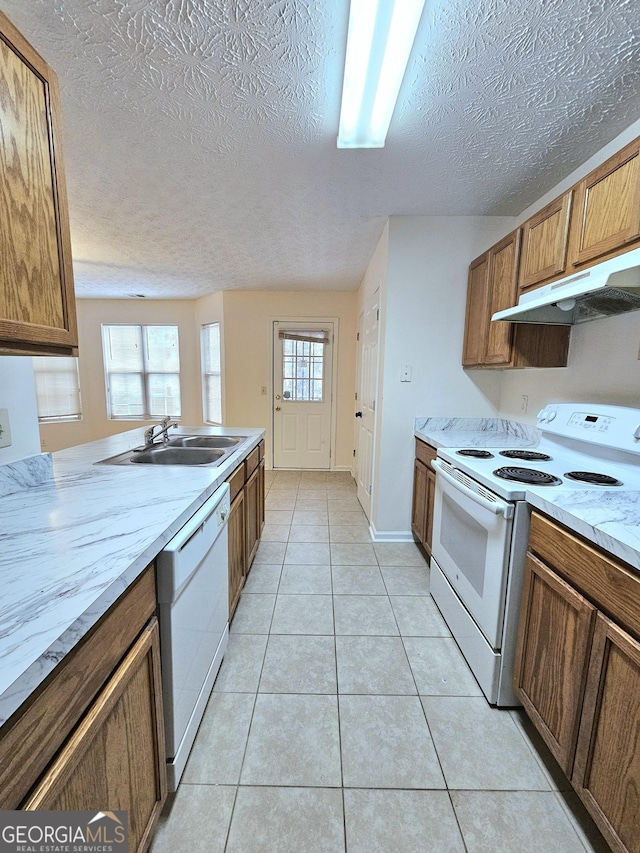 kitchen with a textured ceiling, light tile patterned flooring, white appliances, and sink