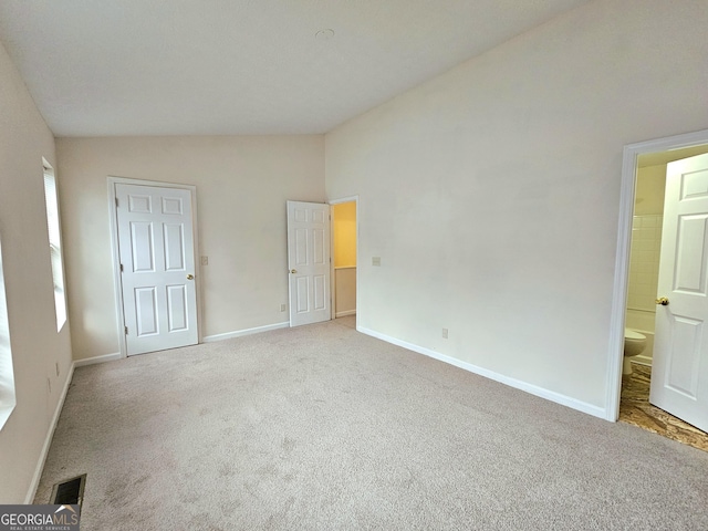 unfurnished bedroom featuring ensuite bathroom, lofted ceiling, and light carpet