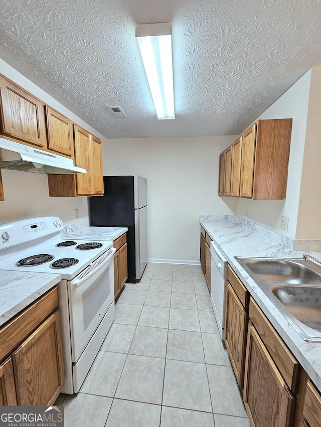 kitchen with a textured ceiling, light tile patterned flooring, white appliances, and sink