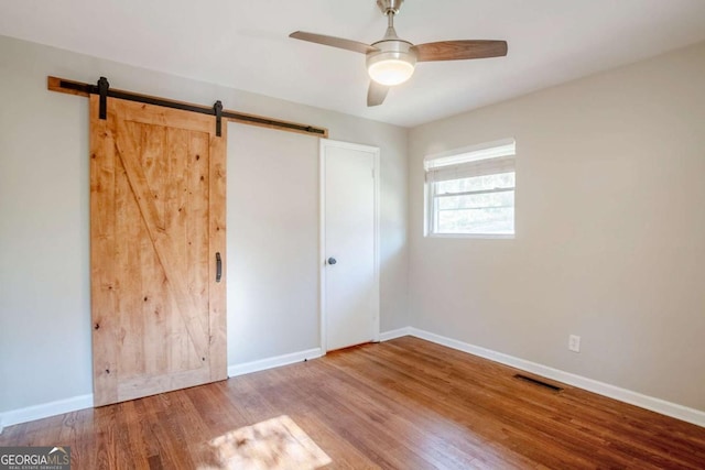 unfurnished bedroom with ceiling fan, a barn door, and wood-type flooring