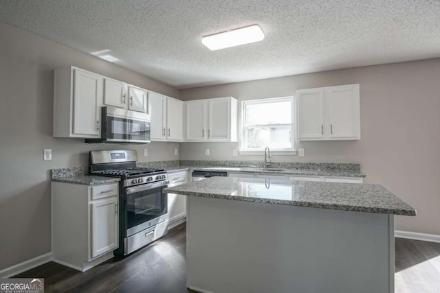 kitchen with light stone counters, stainless steel appliances, a kitchen island, sink, and white cabinetry