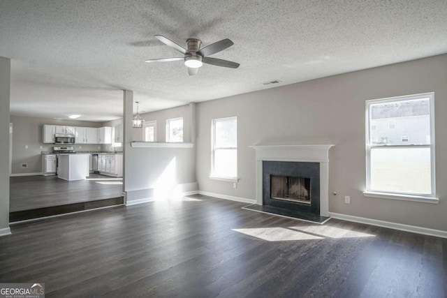 unfurnished living room featuring ceiling fan with notable chandelier, a healthy amount of sunlight, and dark hardwood / wood-style floors