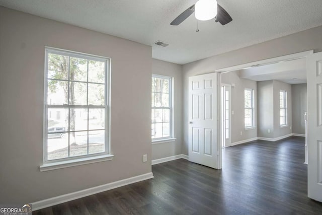 unfurnished room with a textured ceiling, a wealth of natural light, dark wood-type flooring, and ceiling fan