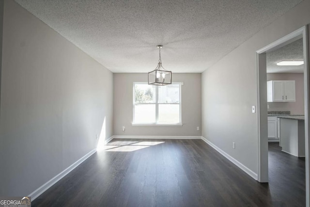 unfurnished room with a textured ceiling, a chandelier, and dark hardwood / wood-style floors