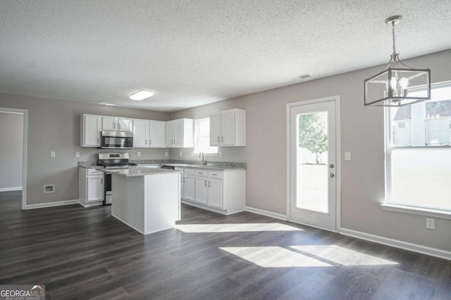 kitchen with dark wood-type flooring, hanging light fixtures, white cabinets, a kitchen island, and appliances with stainless steel finishes