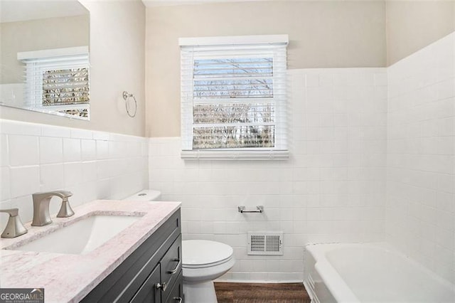 bathroom with a bathing tub, vanity, toilet, and tile walls