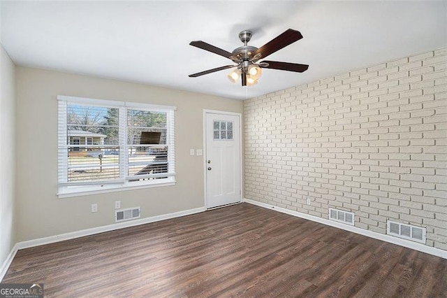 empty room featuring dark hardwood / wood-style flooring, ceiling fan, and brick wall