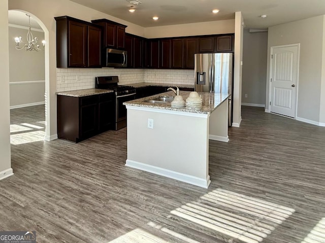 kitchen featuring decorative backsplash, appliances with stainless steel finishes, light stone counters, a kitchen island with sink, and sink